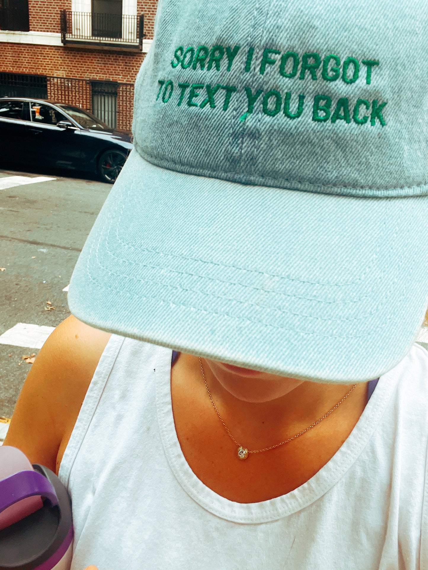 Person wearing a light blue cap with text 'Sorry I forgot to text you back' on a street.