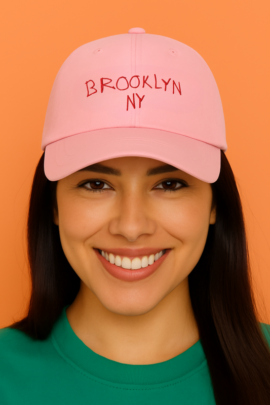 Woman wearing a pink cap with 'Brooklyn NY' text against an orange background