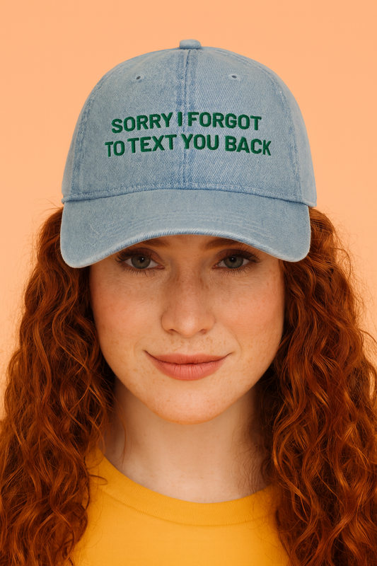 Person wearing a denim cap with text 'SORRY I FORGOT TO TEXT YOU BACK' on an orange background